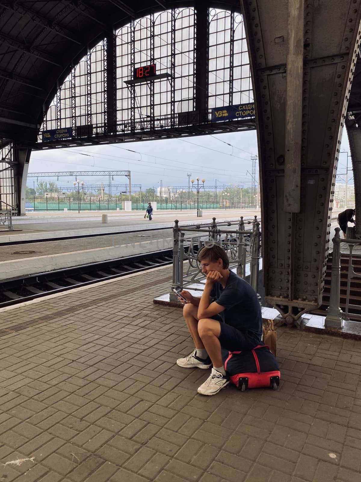 young man sitting on a bag on the railway station and watching on the mobile phone