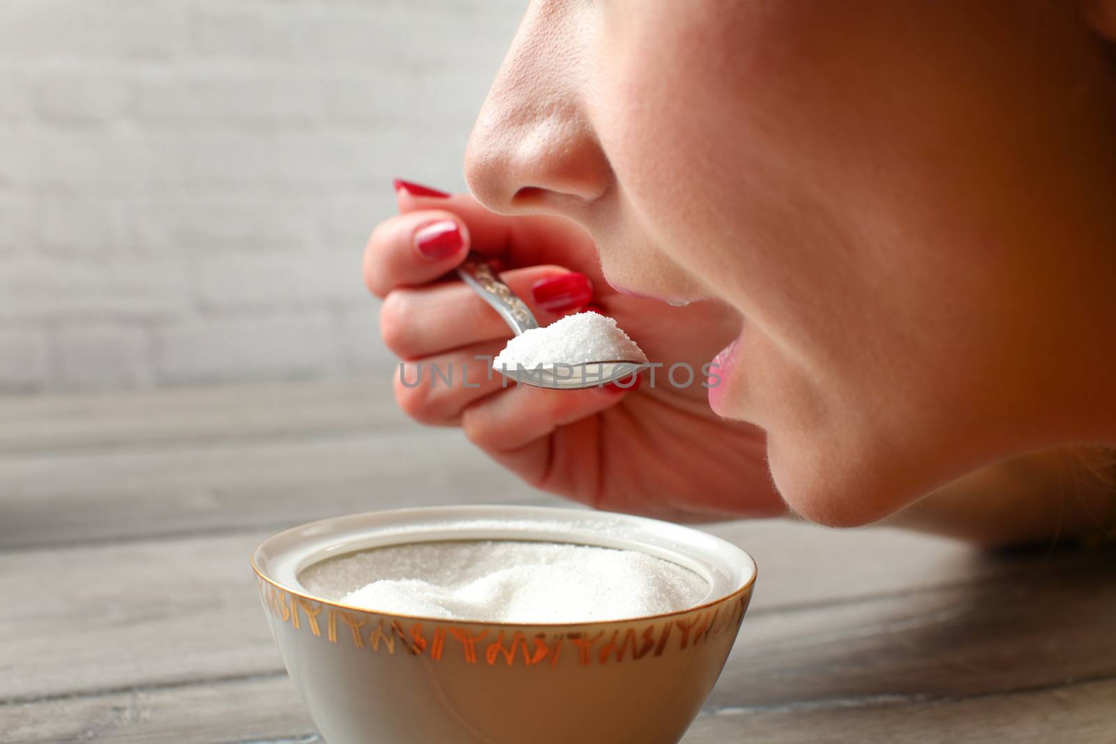 Detail on mouth of woman about to eat spoon full of sugar from small sugar bowl. Overuse of fructose concept.