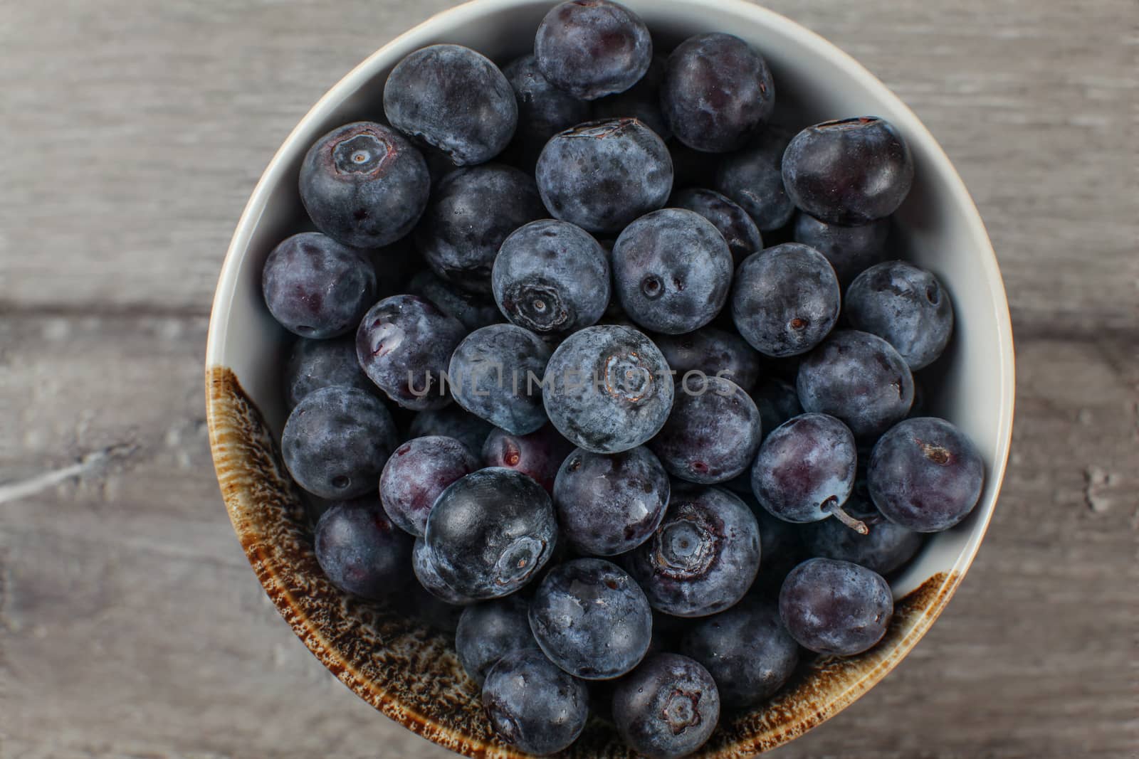 Close up detail of small bowl filled with blueberries seen from above, placed on gray wood desk.