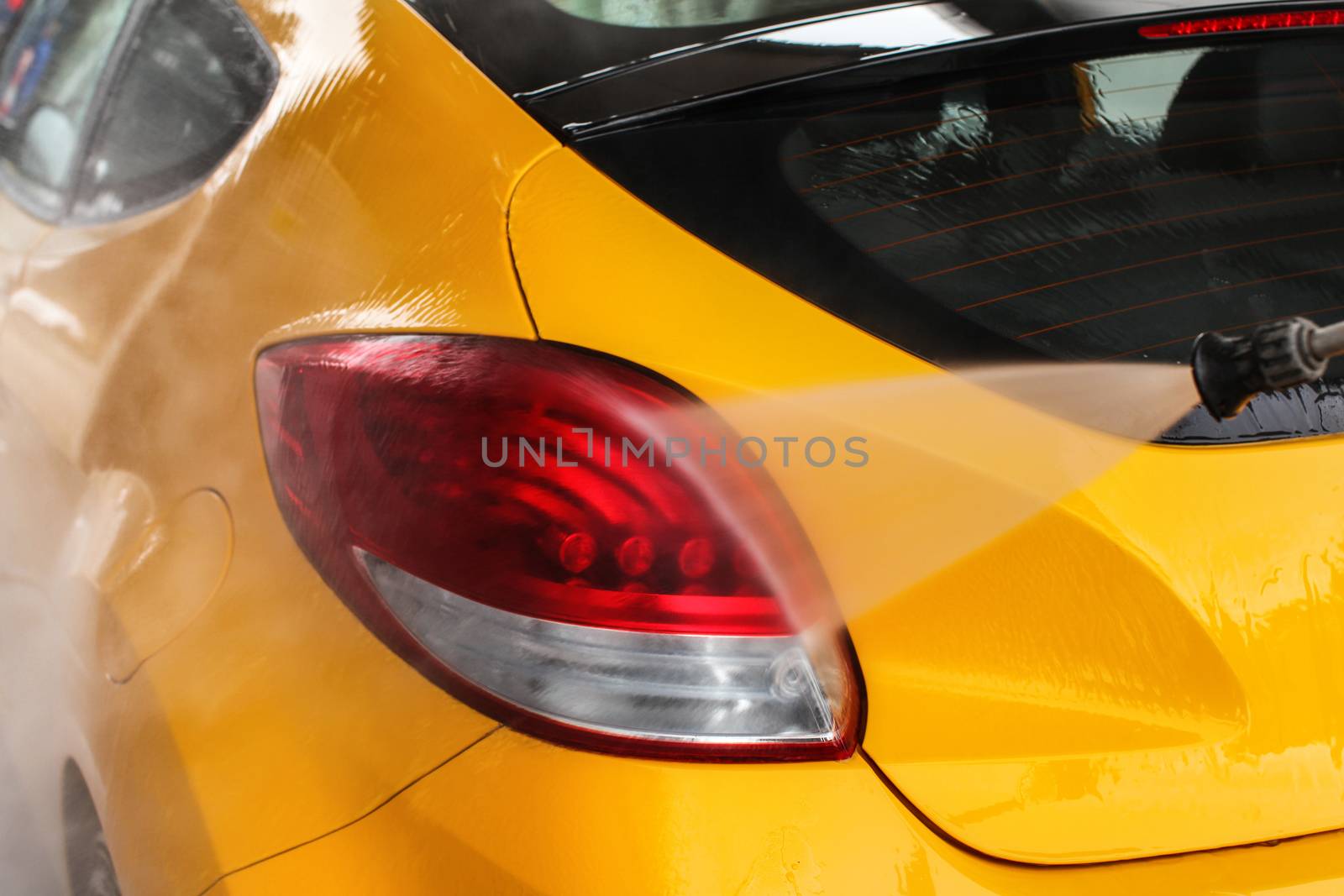 Detail on yellow car rear light being washed in carwash.