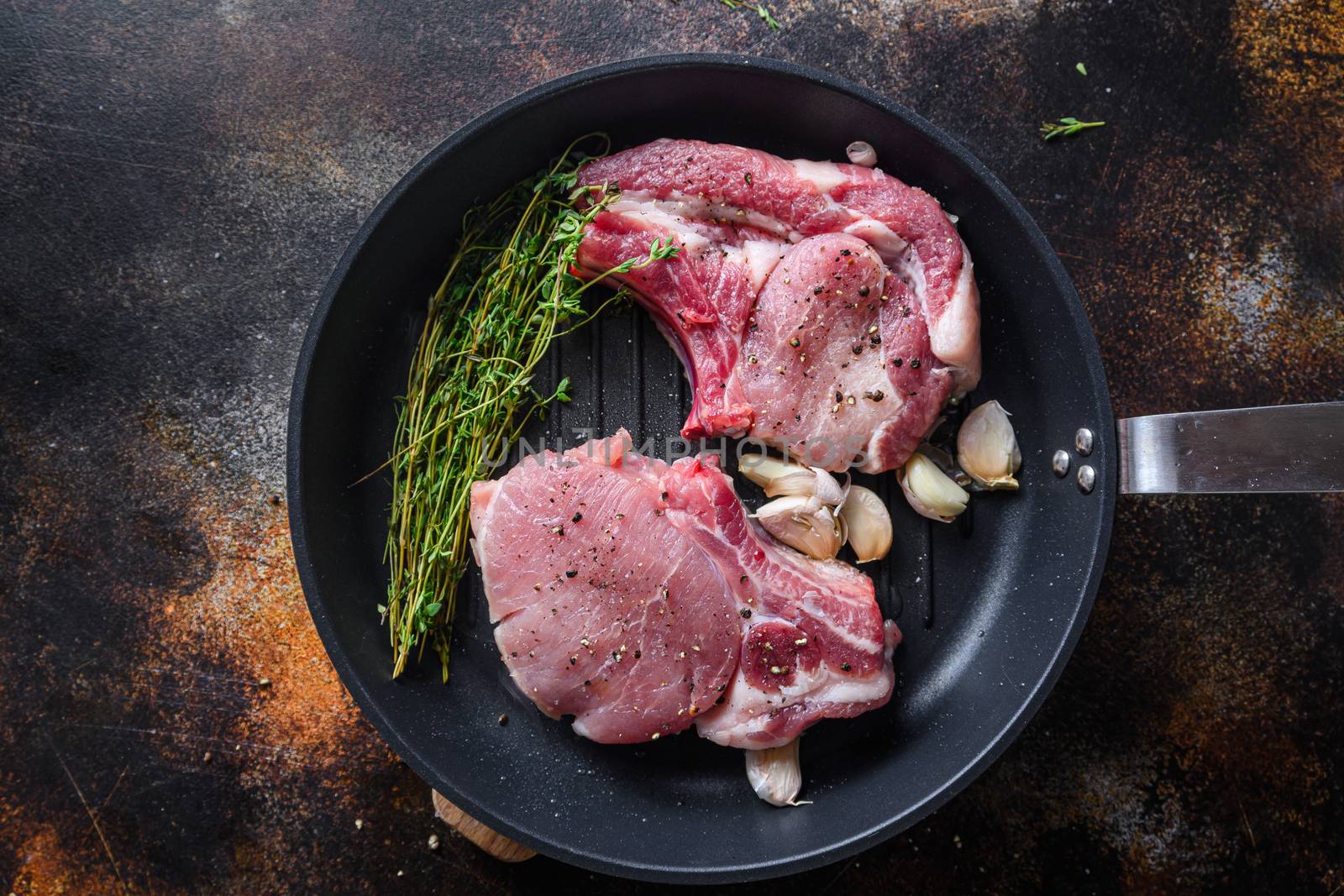 Juicy grilled pork steak with herbs on bone in grill frying pan hot with smoke and hot oil just from fire, top view cooking bone with seasonings rustic metal background.