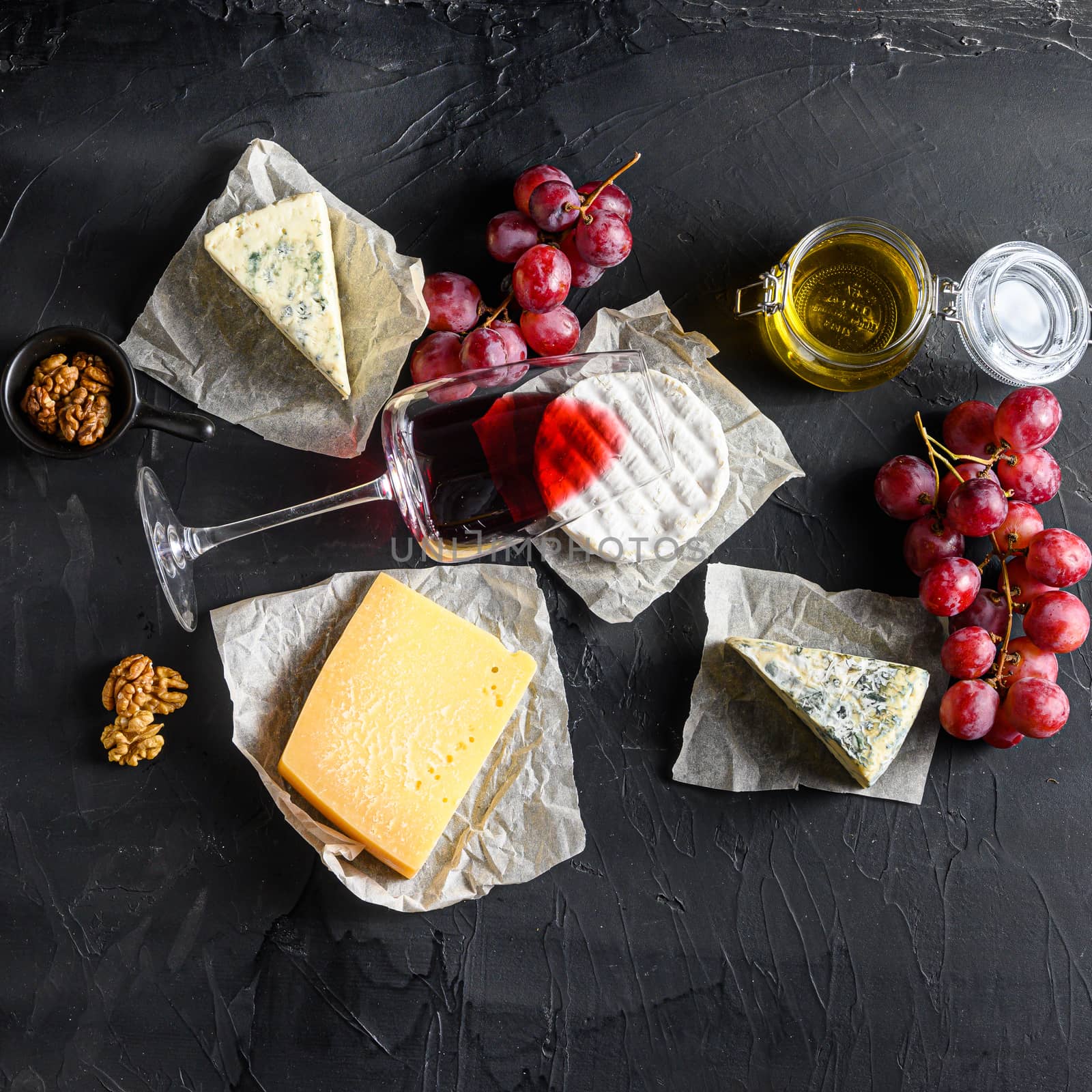 Grapes, red wine, cheeses, brie cheese , blue, chease honey and nuts over black background top view. Square.