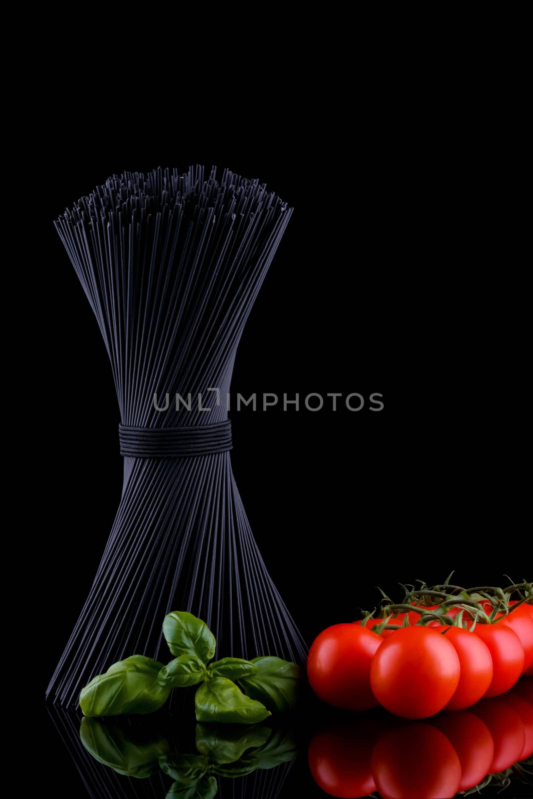 Black spaghetti with basel leaves and red tomato on black background by Fischeron