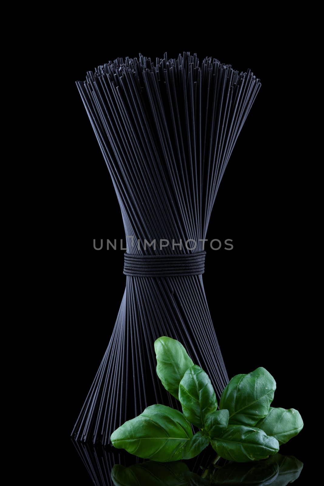 Black spaghetti with basel leaves on black background.