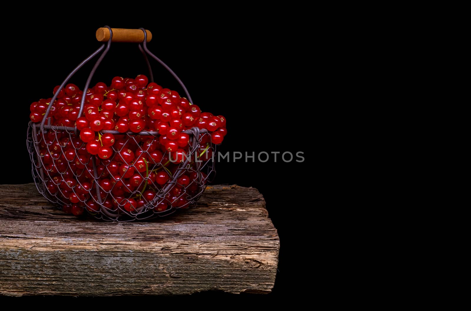 Red currant in a metal basket on black background.