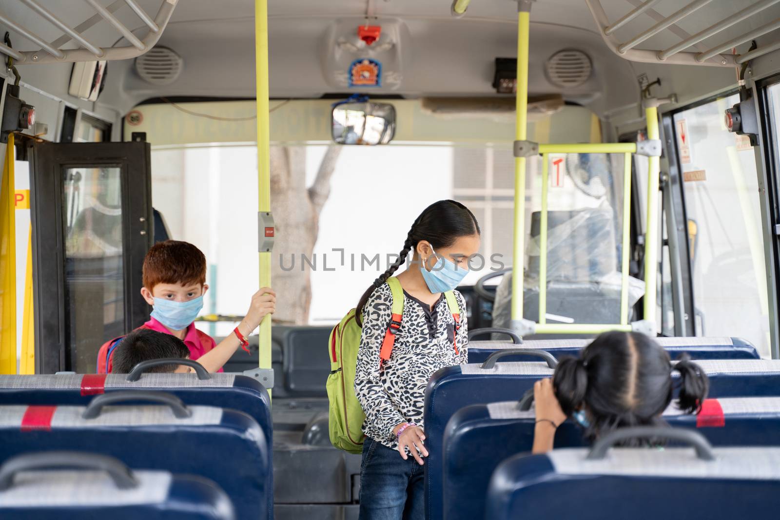 Kids with medical mask coming inside school bus and sitting on seats while maintaining social distance due to coronavirus or covid-19 pandemic - Concept of school reopen or back to school by lakshmiprasad.maski@gmai.com