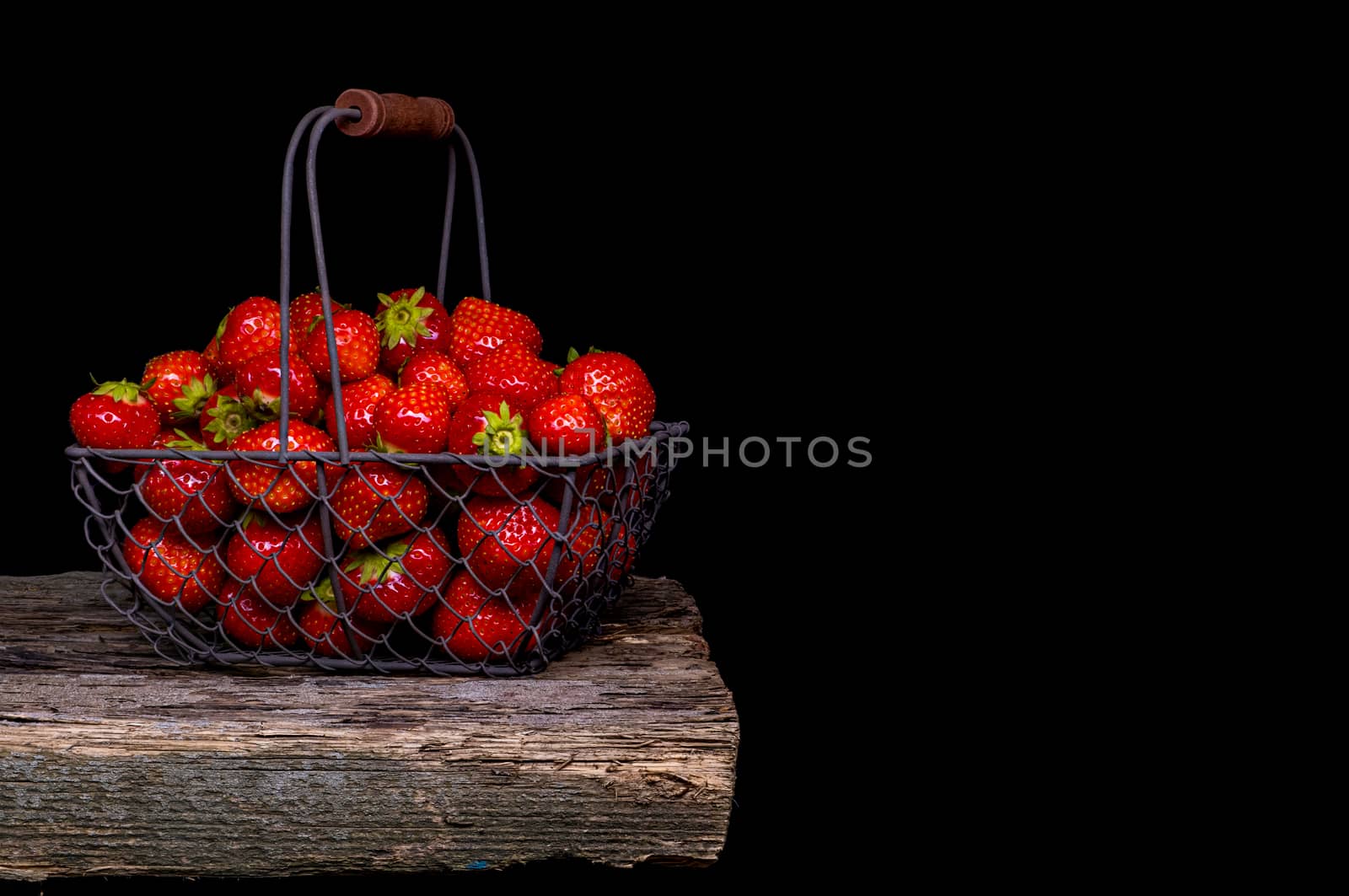 Strawberry with strawberry leaf in a metal basket on black background.