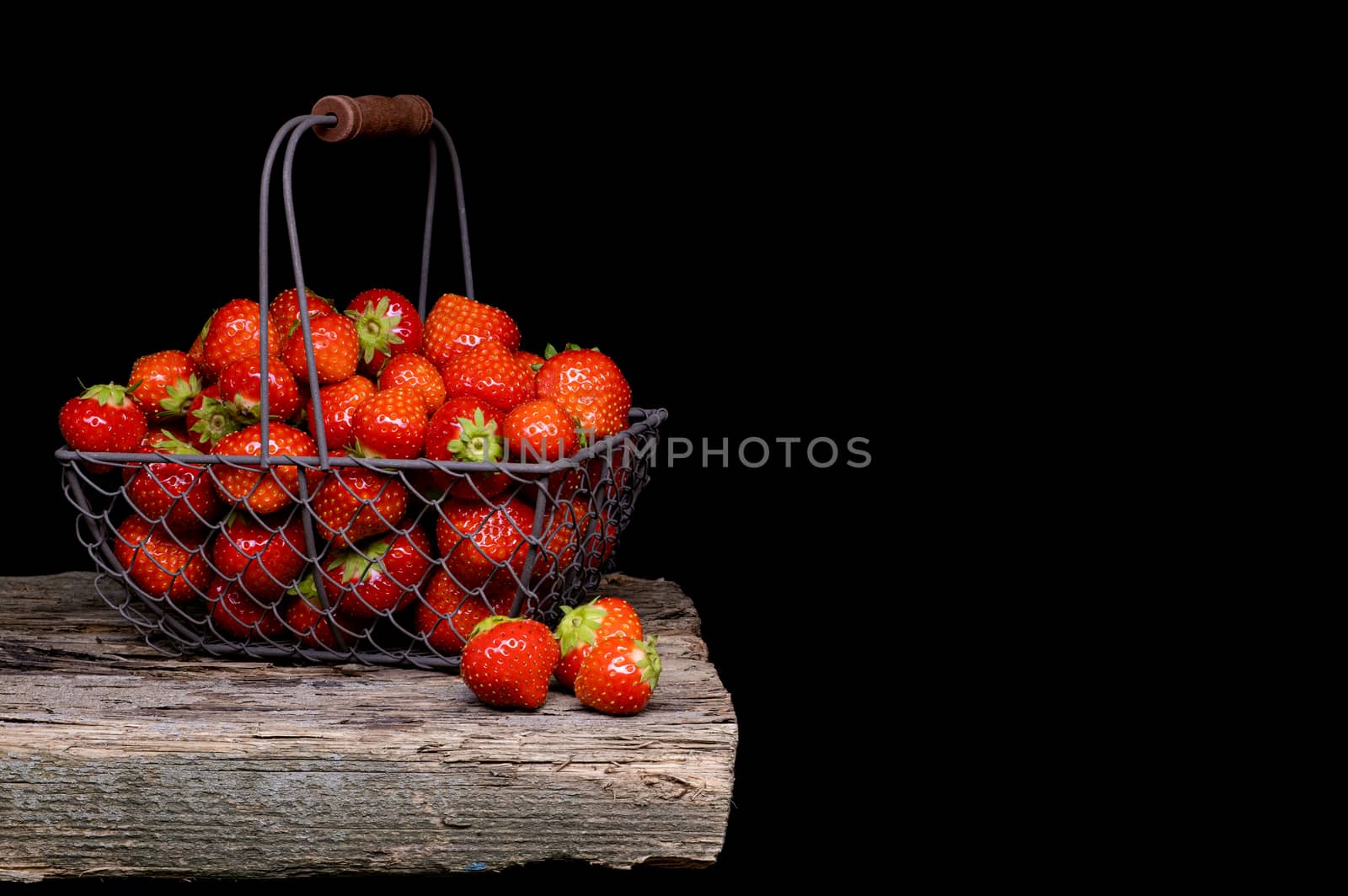 Strawberry with strawberry leaf in a metal basket on black background.