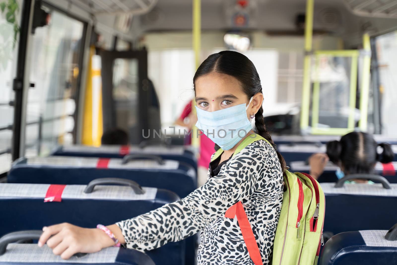 Portrait of Girl kid student in medical mask inside the school bus looking at camera - Concept of school reopen or back to school with new normal lifestyle by lakshmiprasad.maski@gmai.com