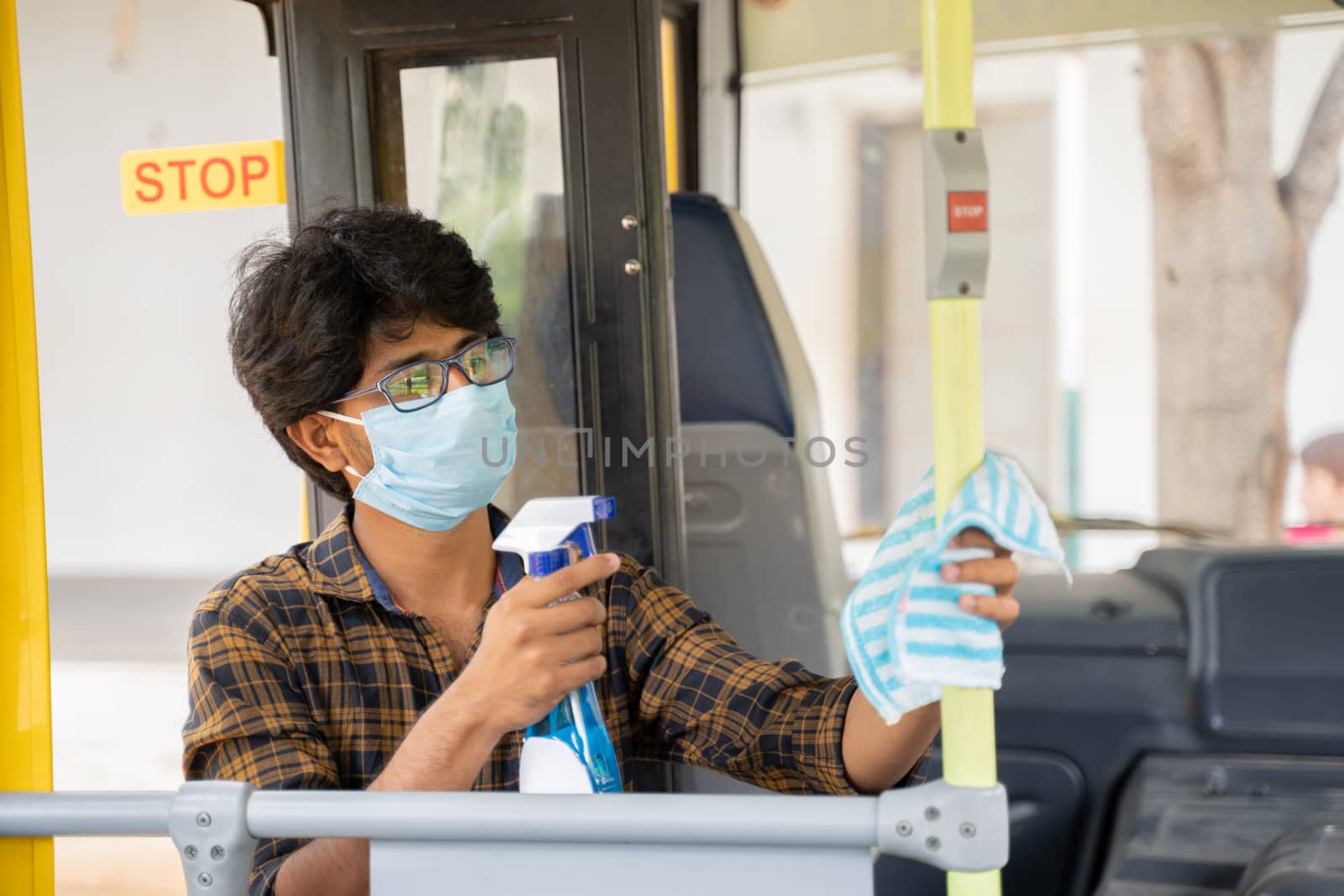 Young man in medical mask disinfecting or sanitizing bus by using alcohol Disinfectant spray to protect people from coronavirus or covid-19 infection. by lakshmiprasad.maski@gmai.com