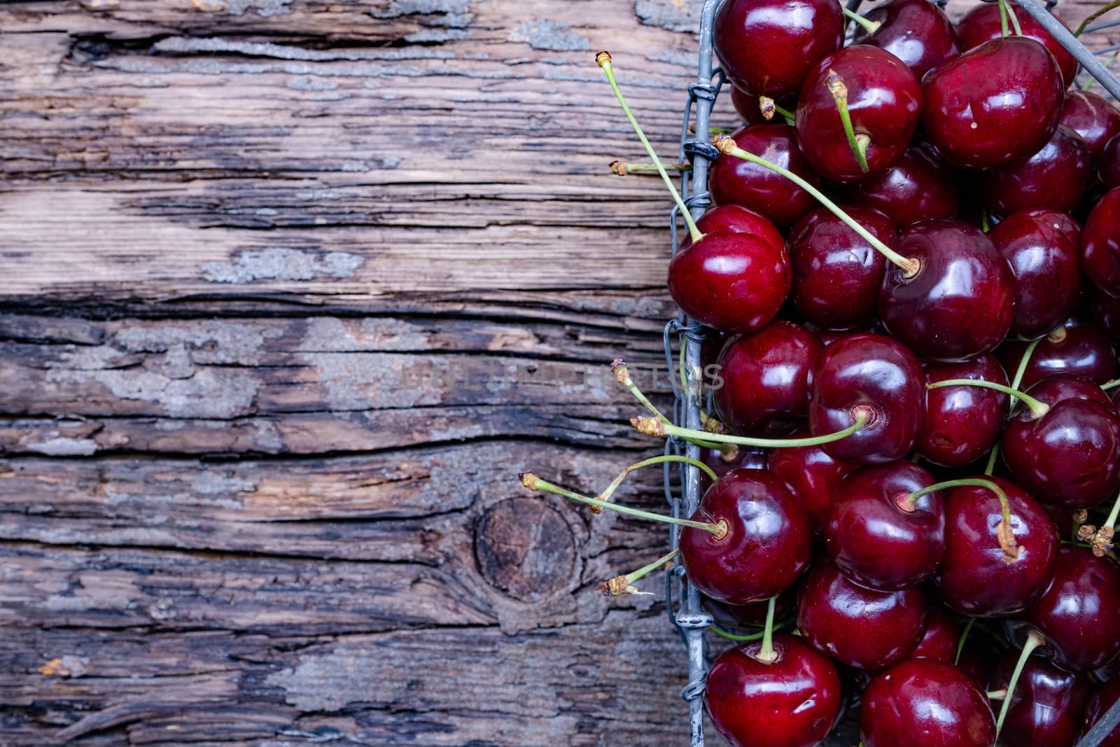 Fresh cherry fruit in a metal basket, top view on old wooden background.