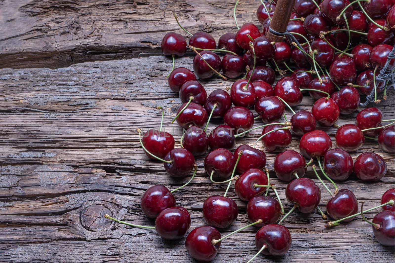 Fresh cherry fruit in a metal basket, top view on old wooden background.