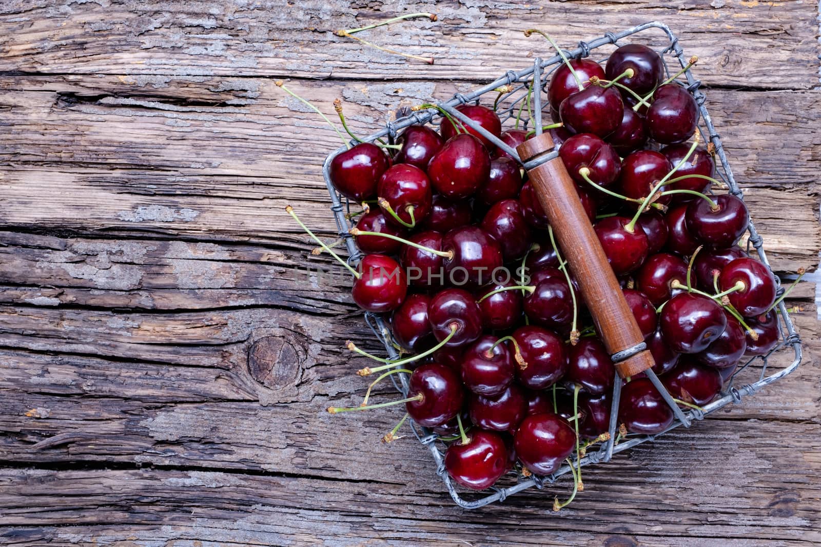 Fresh cherry fruit in a metal basket, top view on old wooden background.