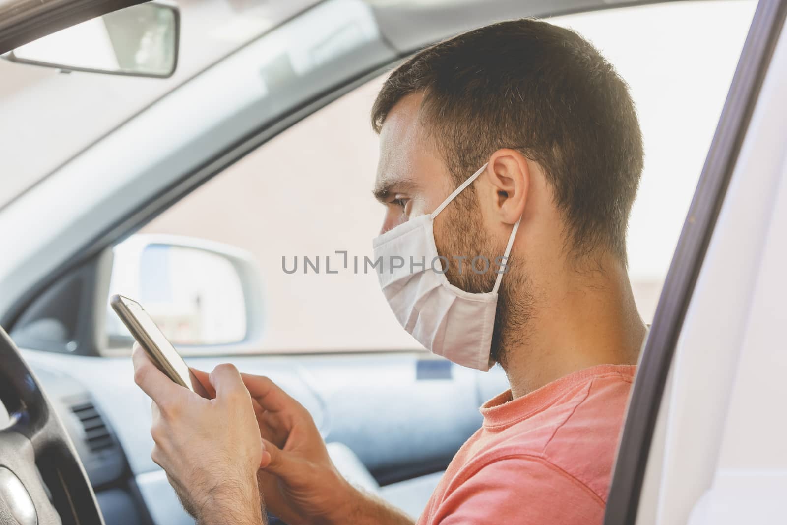 A young man, wearing a cloth face mask, checks the mobile phone inside the car, while he waits for someone before drive, in the province of Zaragoza, Spain.