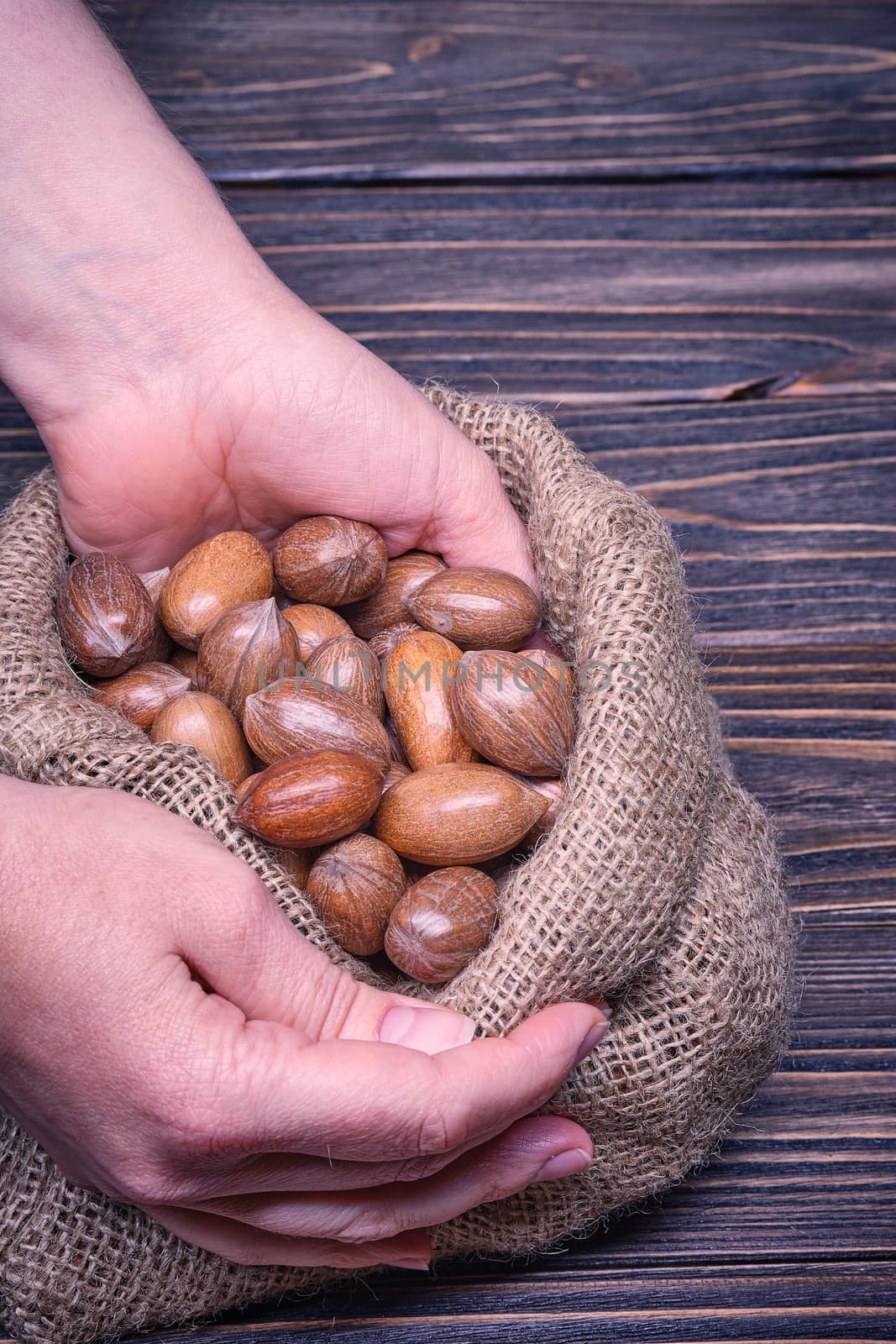Close up woman hand holds pecan nut on a wooden background.