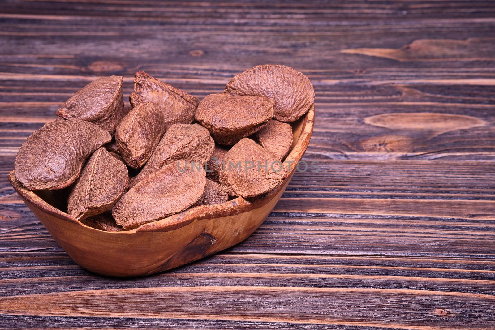 Paranuts in an olive wood cup, vegetarian food in wooden bowls, on old wooden background.