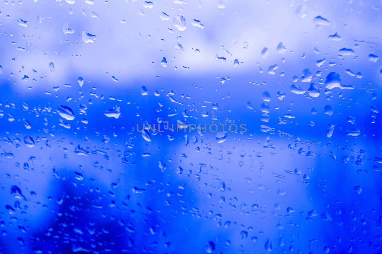 Raindrops on a window, illustrating gray and rainy weather during the day. Blue background. by kb79