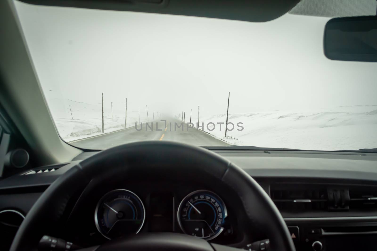 Car interior point of view on road cleared from snow and ice, but piled up on the side of the road. Winter driving.