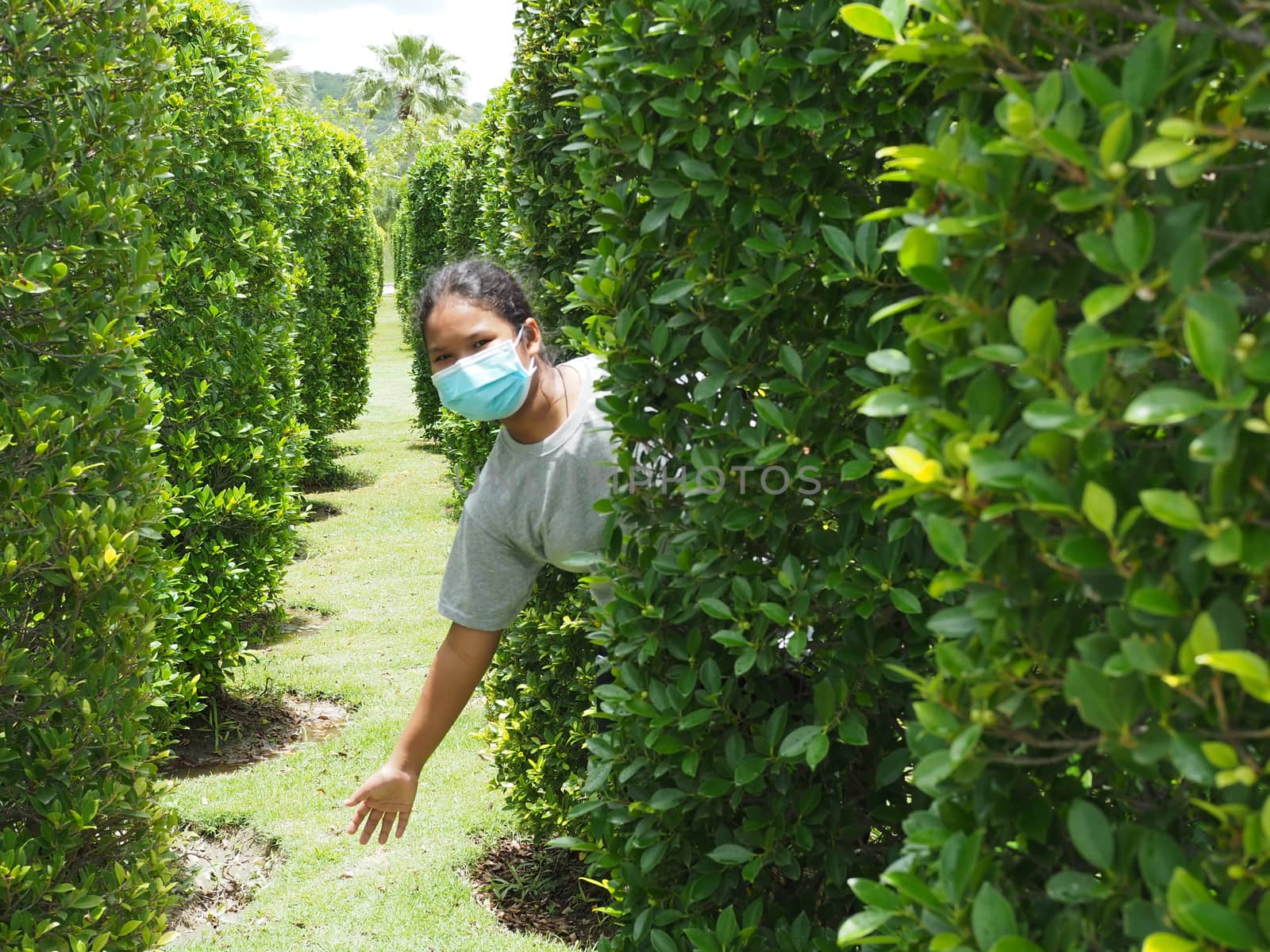 A portrait of a girl wearing a protective mask. On the background is a green bush.