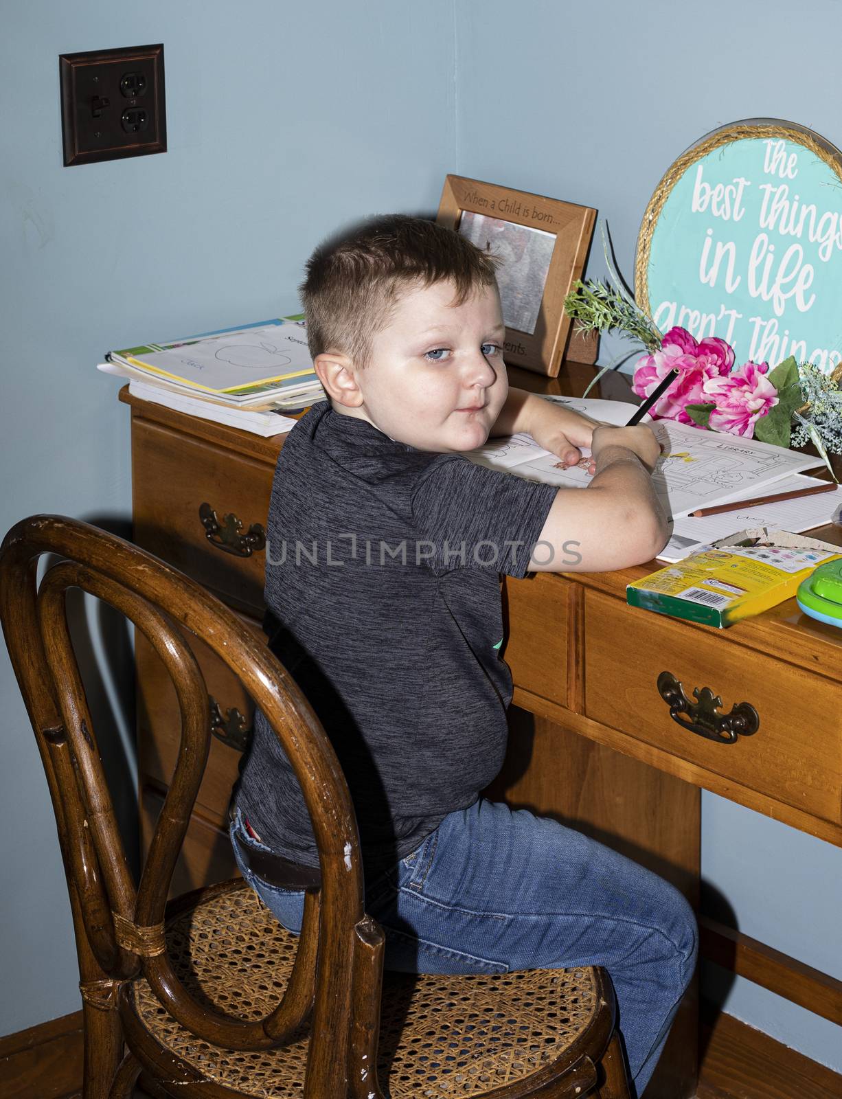 Four-year old pre-kindergarten boy works at his 'school' desk at home during COVID-19 remote class session.