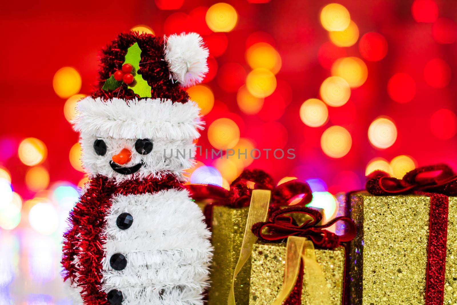 Snowman Christmas figurine near glittery gifts isolated on blurred background of lights. Christmas decorations isolated