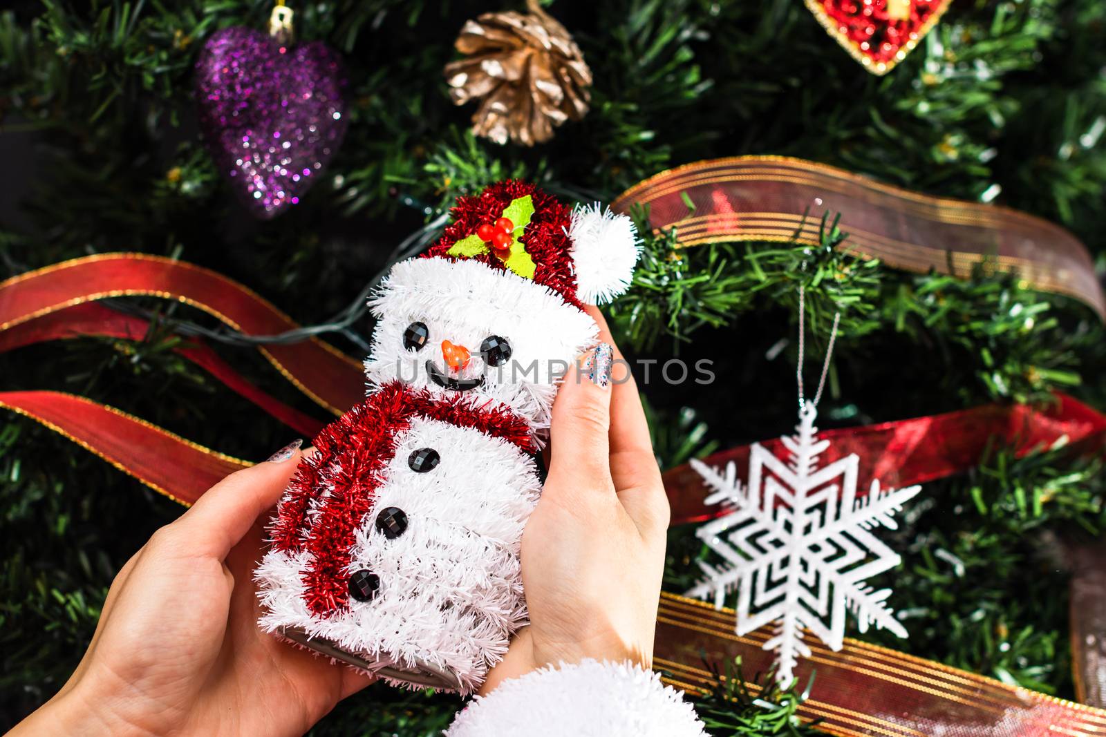 Hands holding Christmas snowman figurine in front of the Christmas tree. Decorating the fir tree isolated