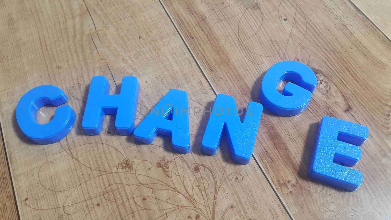 Plastic colored alphabets making words are placed on a wooden floor. These plastic letters can be used for teaching kids.