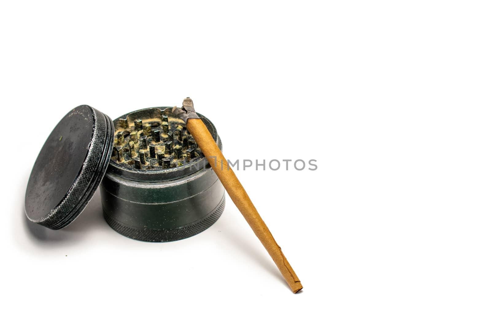 A Lit Cannabis Cigar Leaning on a Black Grinder With the Lid Leaning on the Side