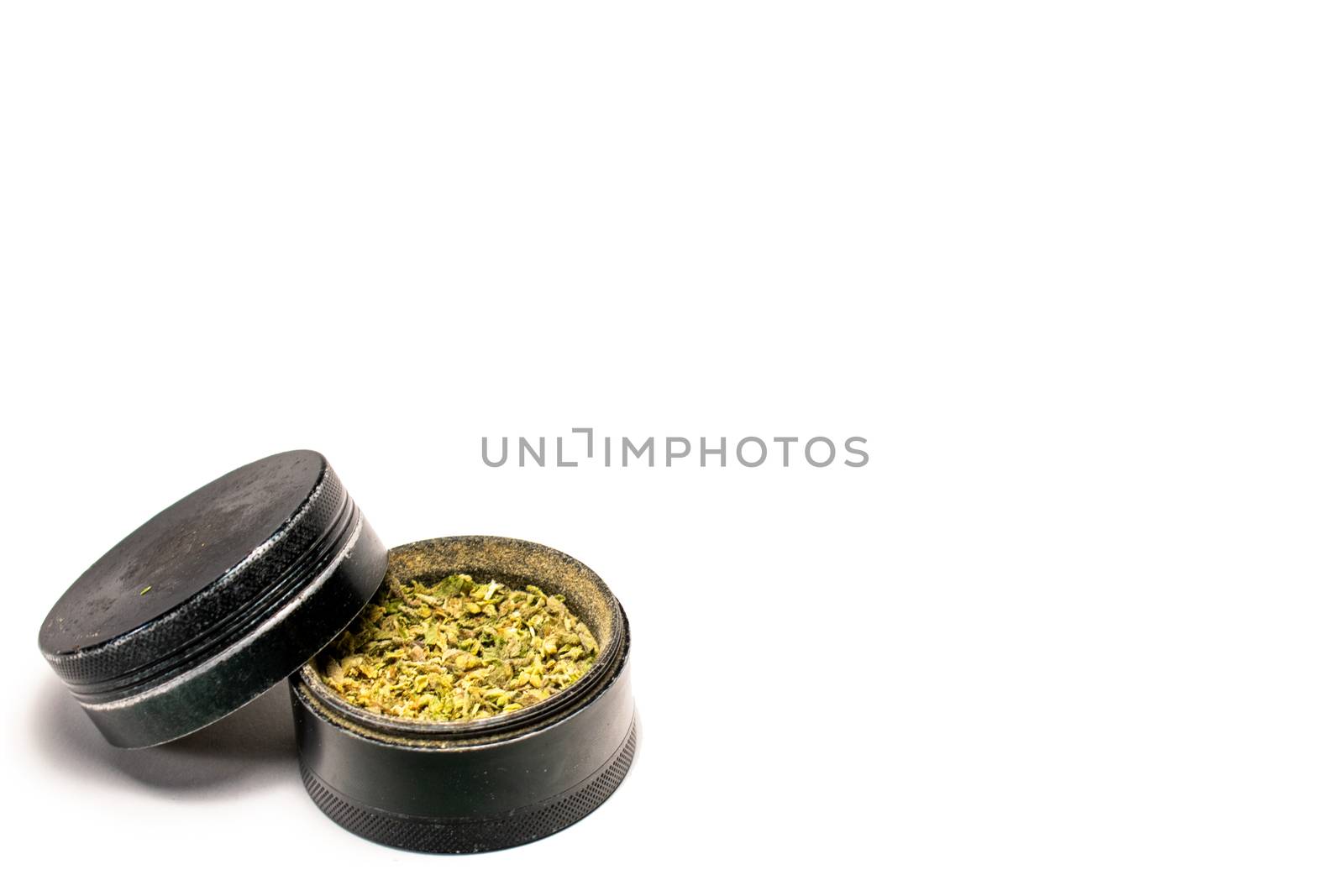 A Black Grinder Full of Green and Orange Cannabis With the Lid Leaning on the Side on a Pure White Background