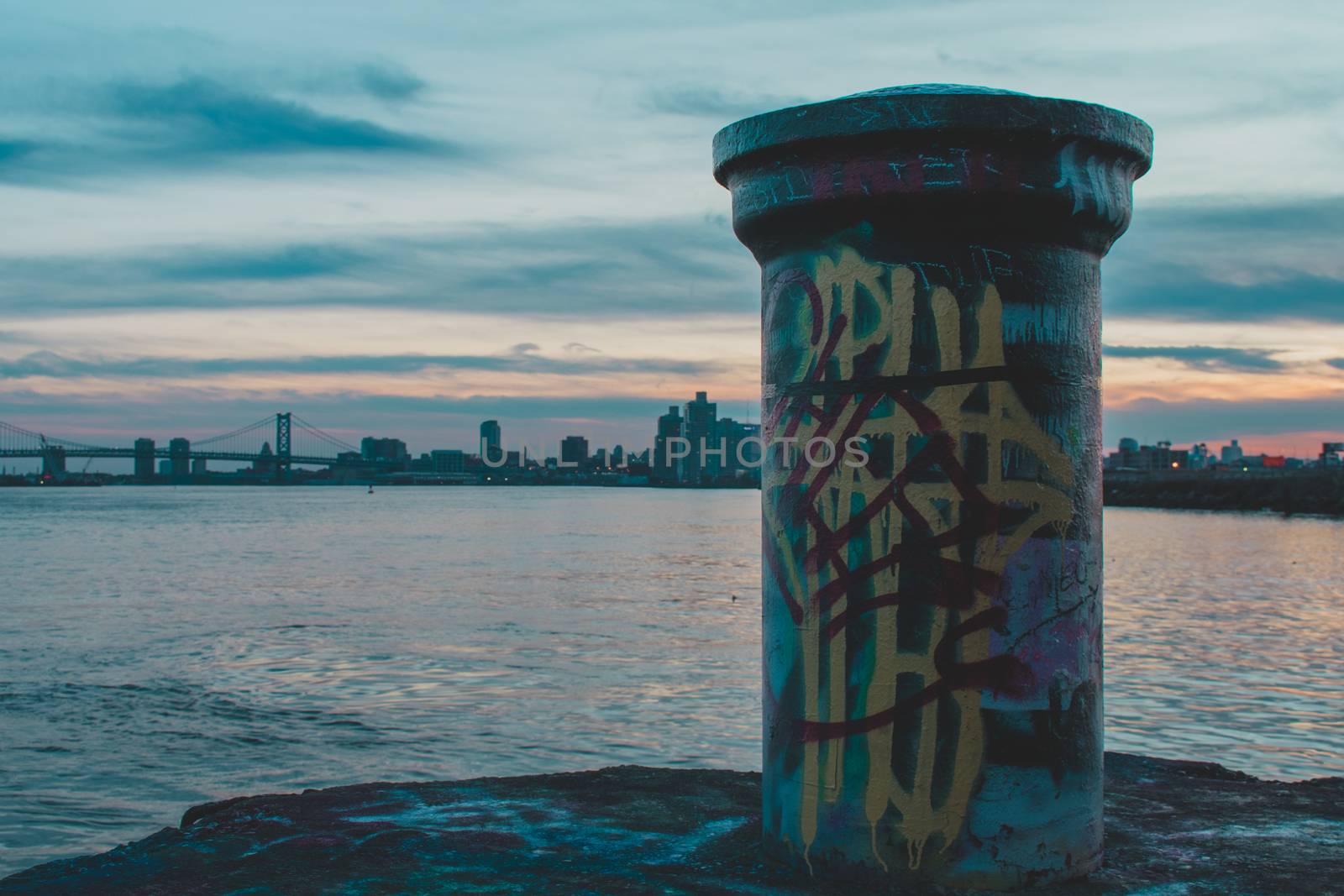 A Graffiti Tagged Pole at Graffiti Pier With the Philadelphia Skyline and a Dramatic Sunset Behind It