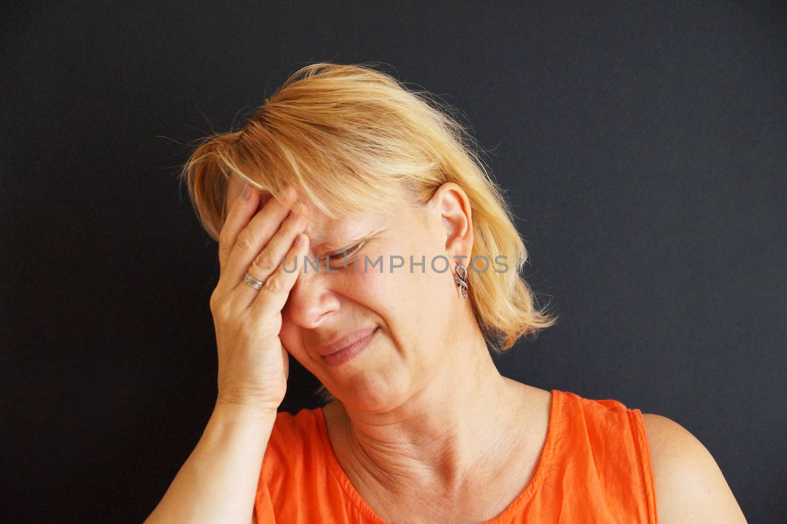 unhappy woman holding her head with her hand, portrait on black background.