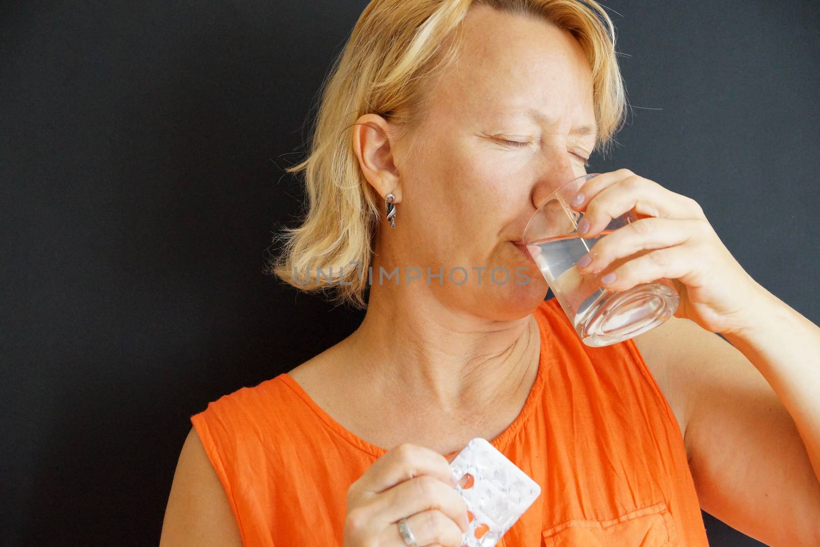 sick woman drinks pills with water, portrait on black background by Annado