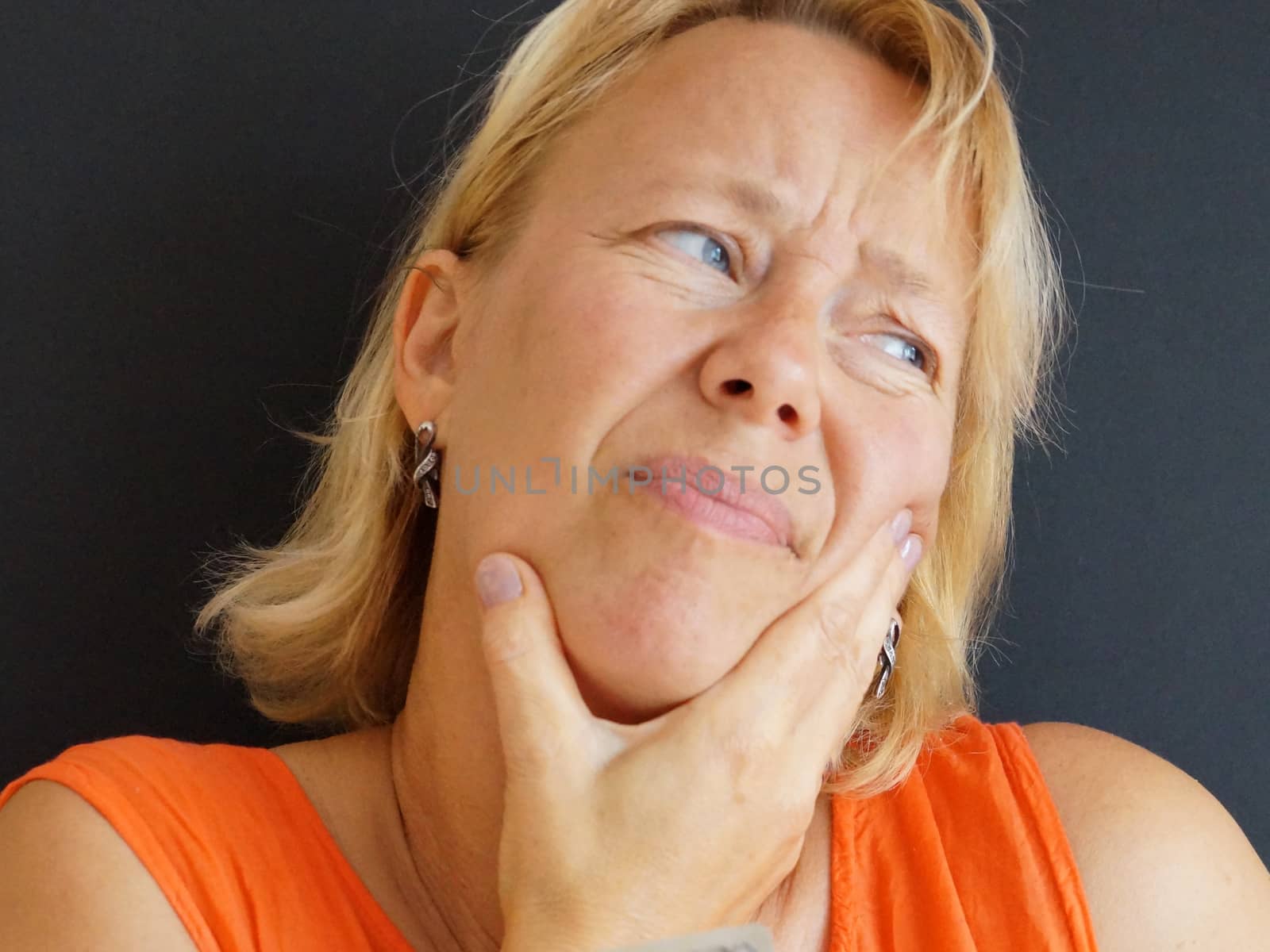 unhappy woman holding her hand for a bad tooth, portrait on black background by Annado