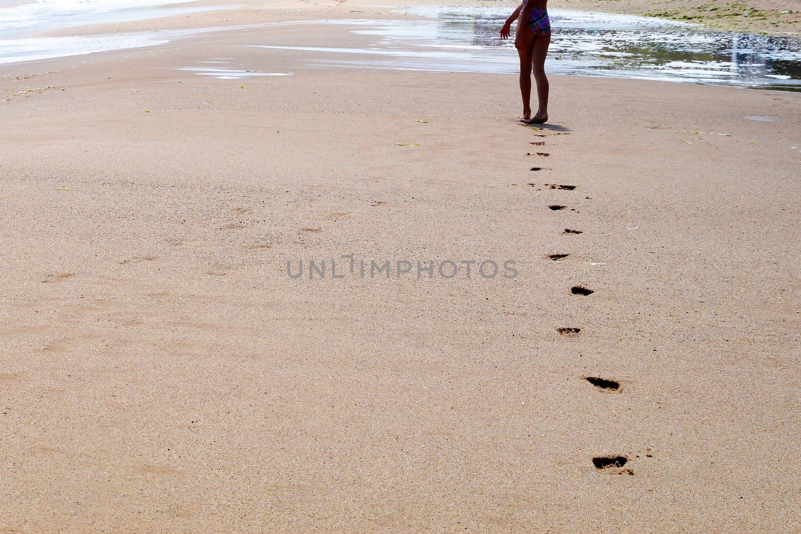 feet of a young girl walk barefoot on a wet beach, leaving footprints in the sand by Annado