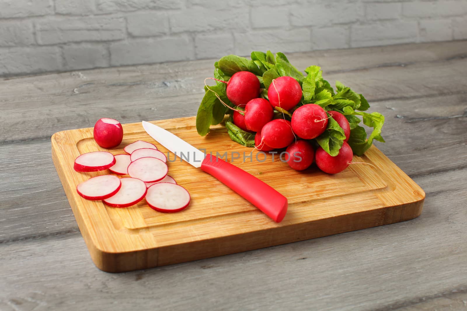 Bunch of fresh red radish on a wooden cutting board, ceramic knife, with some of radish cut in small circles.