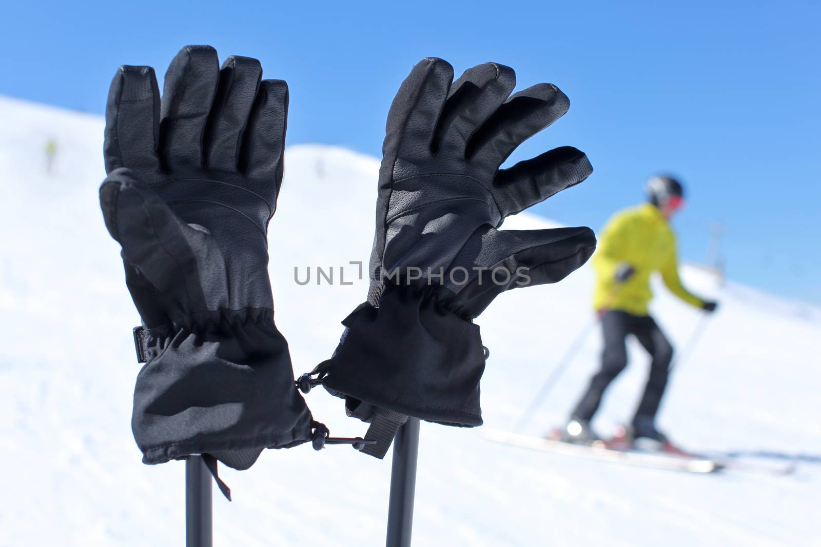 Detail on black ski gloves on ski poles with blurred skier in ba by Ivanko