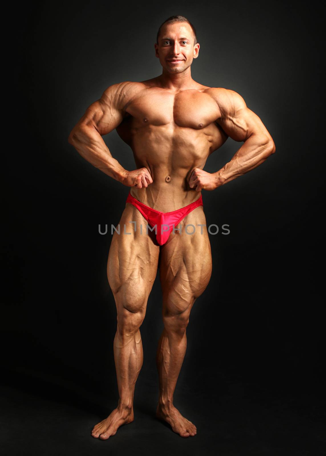 Studio shot of young male bodybuilder, posing, flexing his chest and legs muscles.