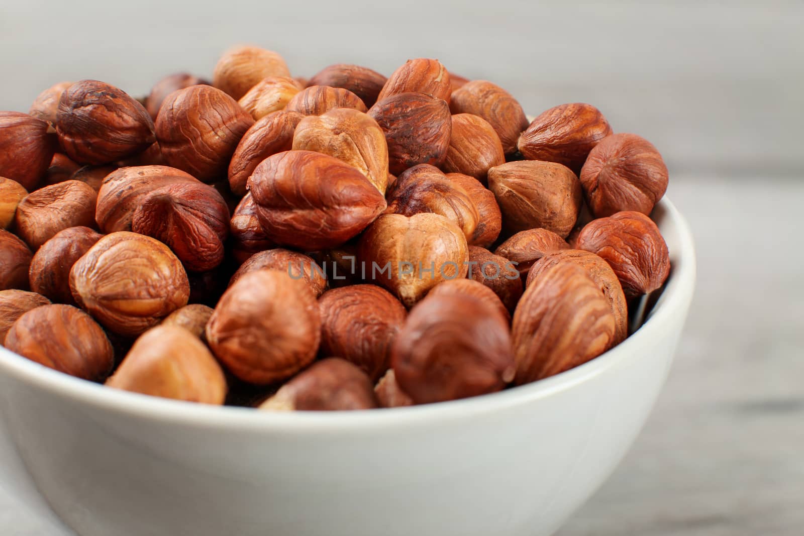 Detail on small white ceramic bowl full of hazelnuts.