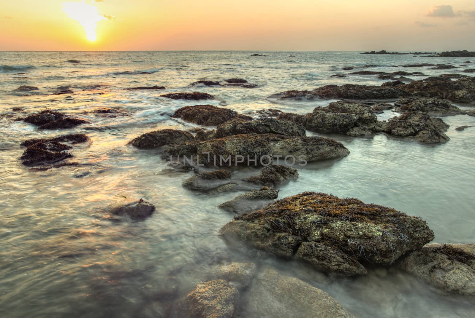 Sunset during low tide on Koh Lanta, Thailand. Algae covered rocks in shallow sea.