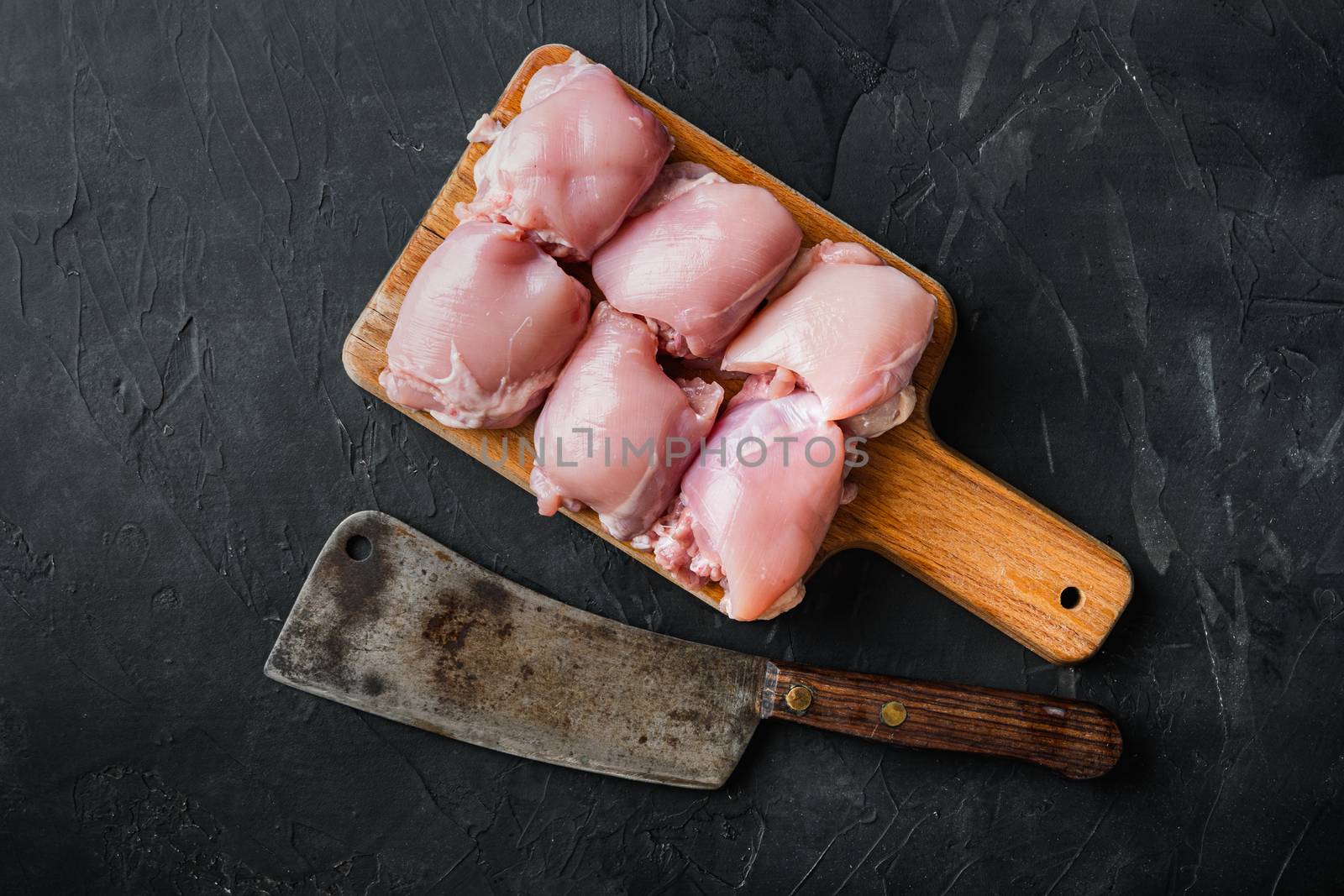 Raw chicken thighs with meat cleaver, on black background, top view.