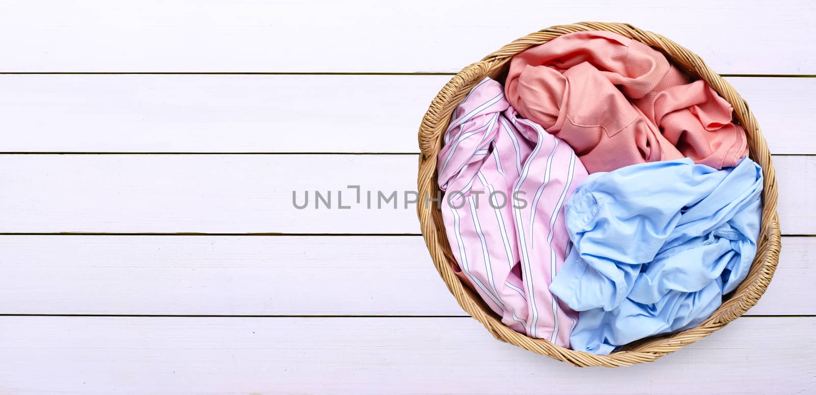 Colorful clothes in laundry basket on white wooden background. Copy space