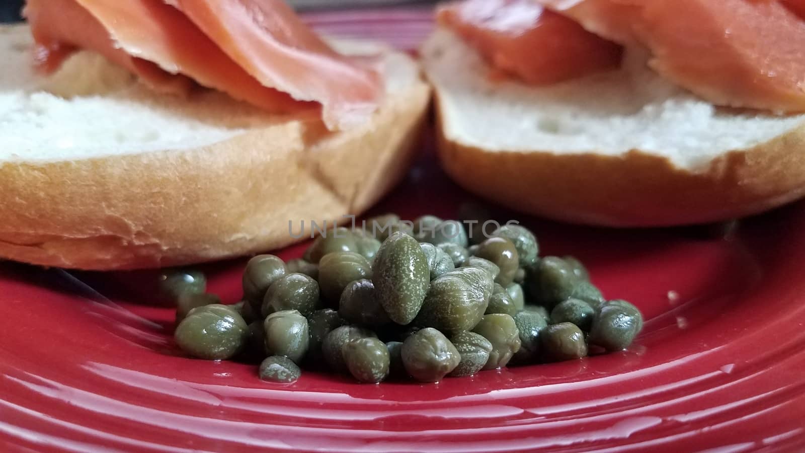 green capers on red plate with bagels and salmon by stockphotofan1