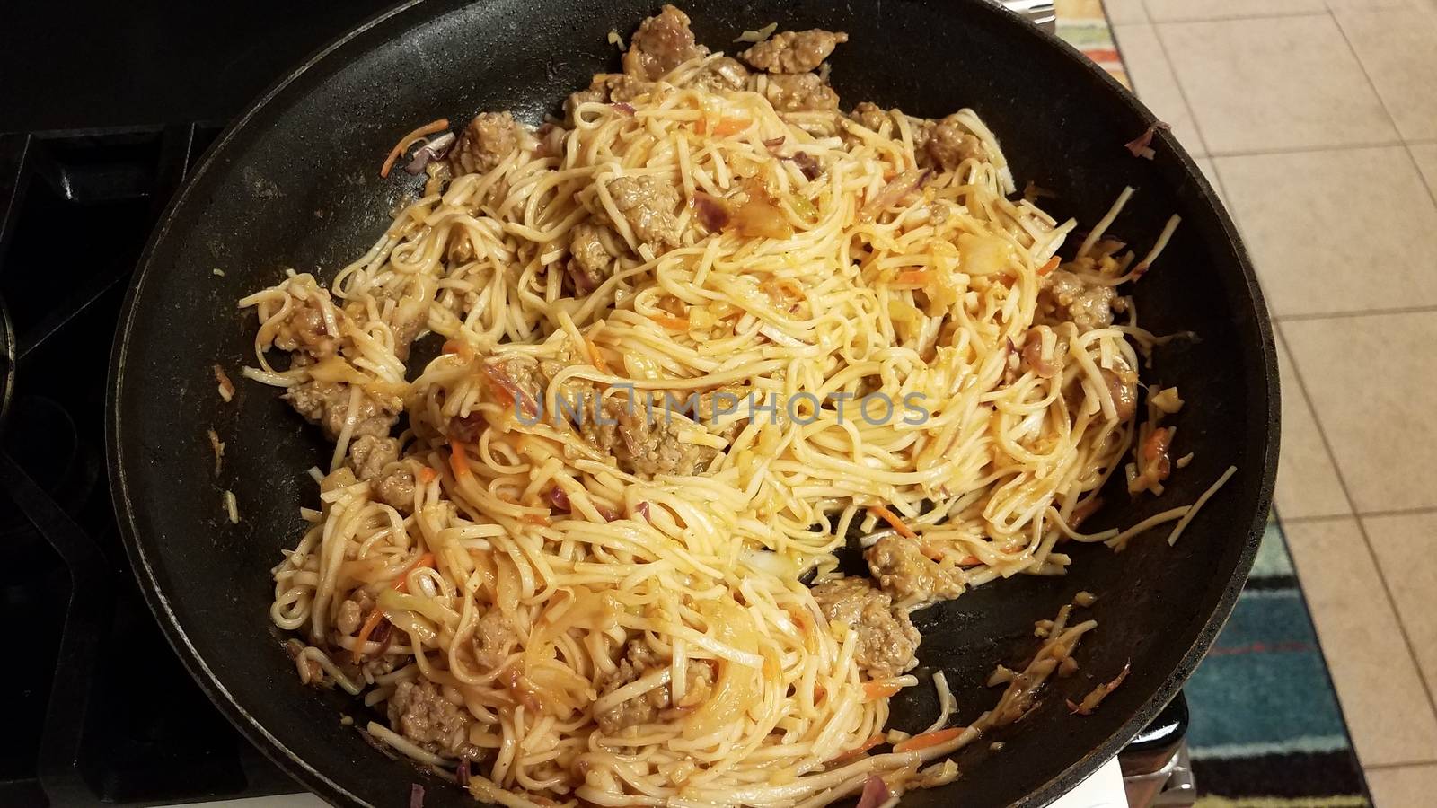 asian noodles and pork in frying pan or skillet on stove