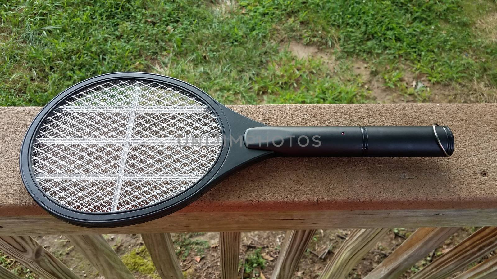 electronic metal tennis racket insect killer on wood deck railing