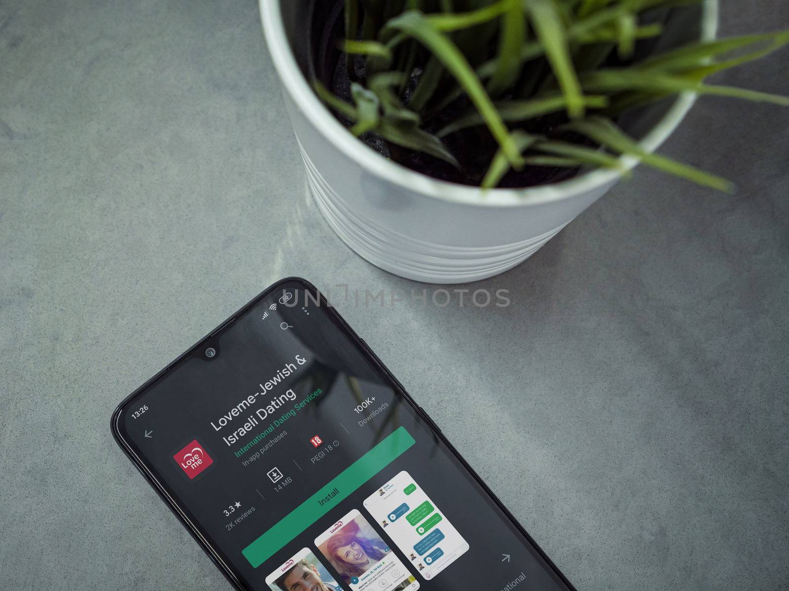 Lod, Israel - July 8, 2020: Modern minimalist office workspace with black mobile smartphone with Loveme app play store page on marble background. Top view flat lay with copy space.