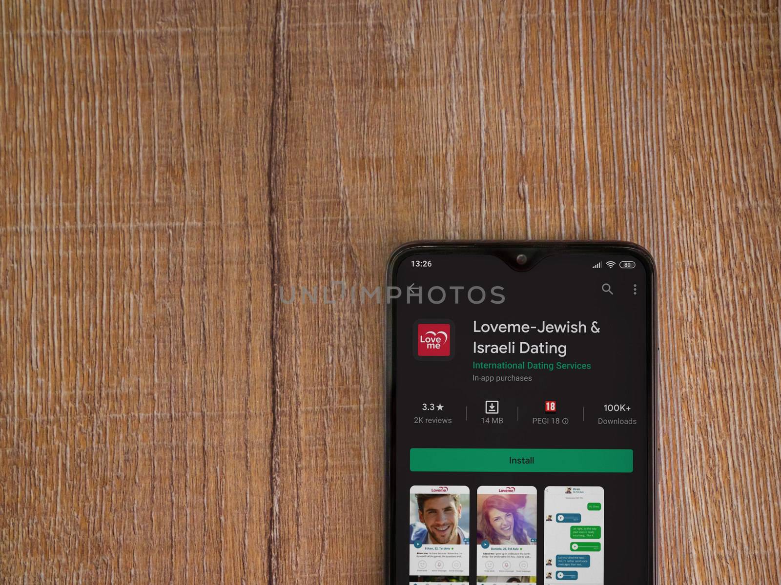 Lod, Israel - July 8, 2020: Loveme app play store page on the display of a black mobile smartphone on wooden background. Top view flat lay with copy space.