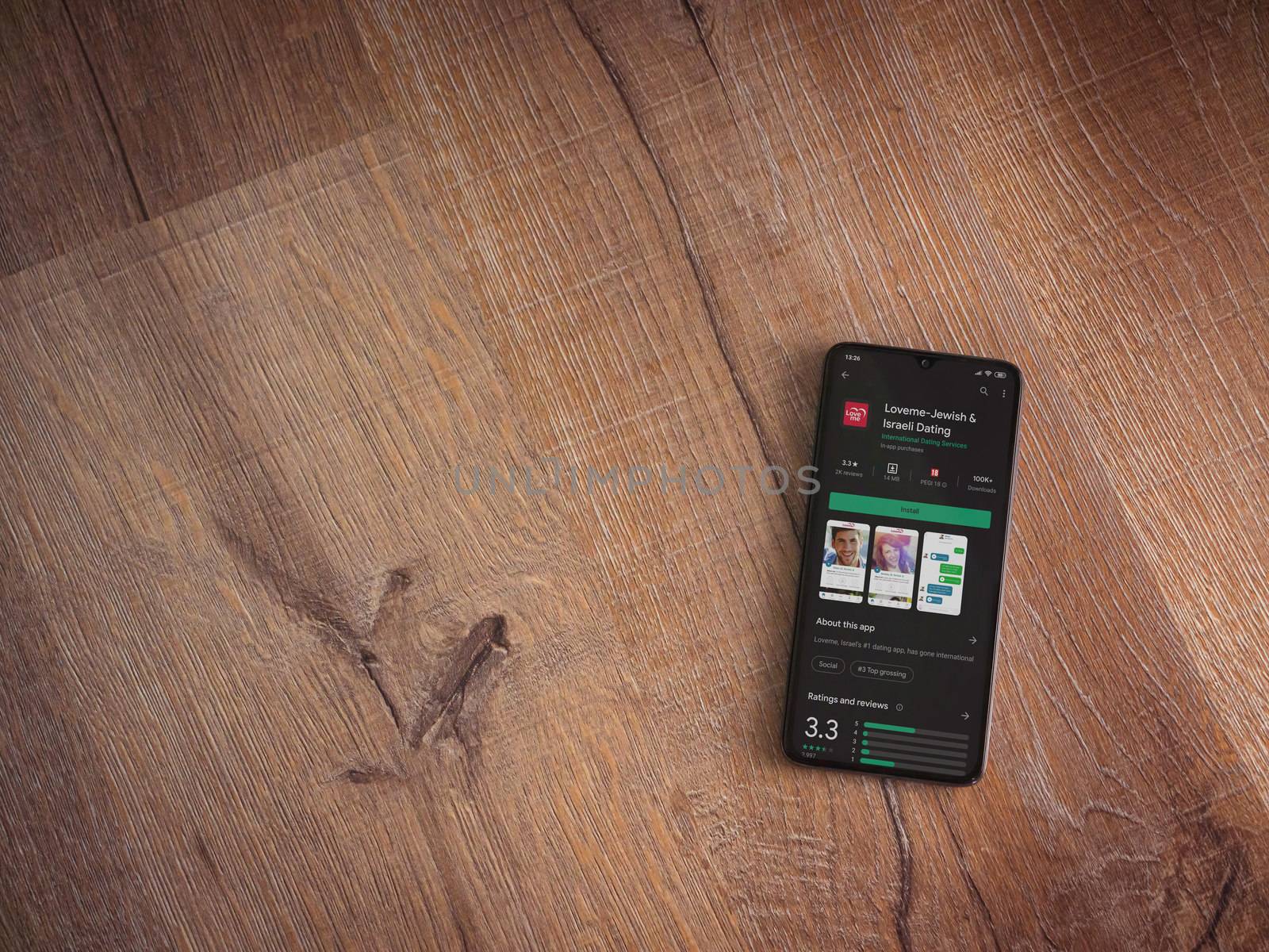 Lod, Israel - July 8, 2020: Loveme app play store page on the display of a black mobile smartphone on wooden background. Top view flat lay with copy space.