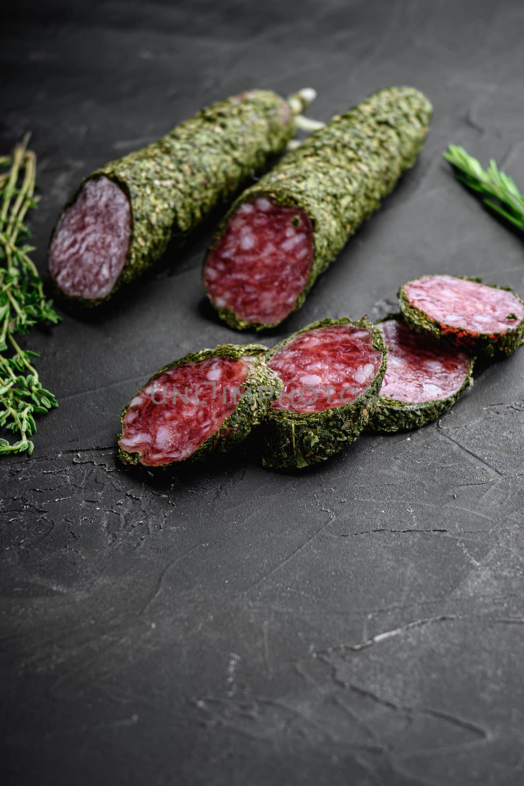 Fuet salami sausage in herbs on black textured surface.