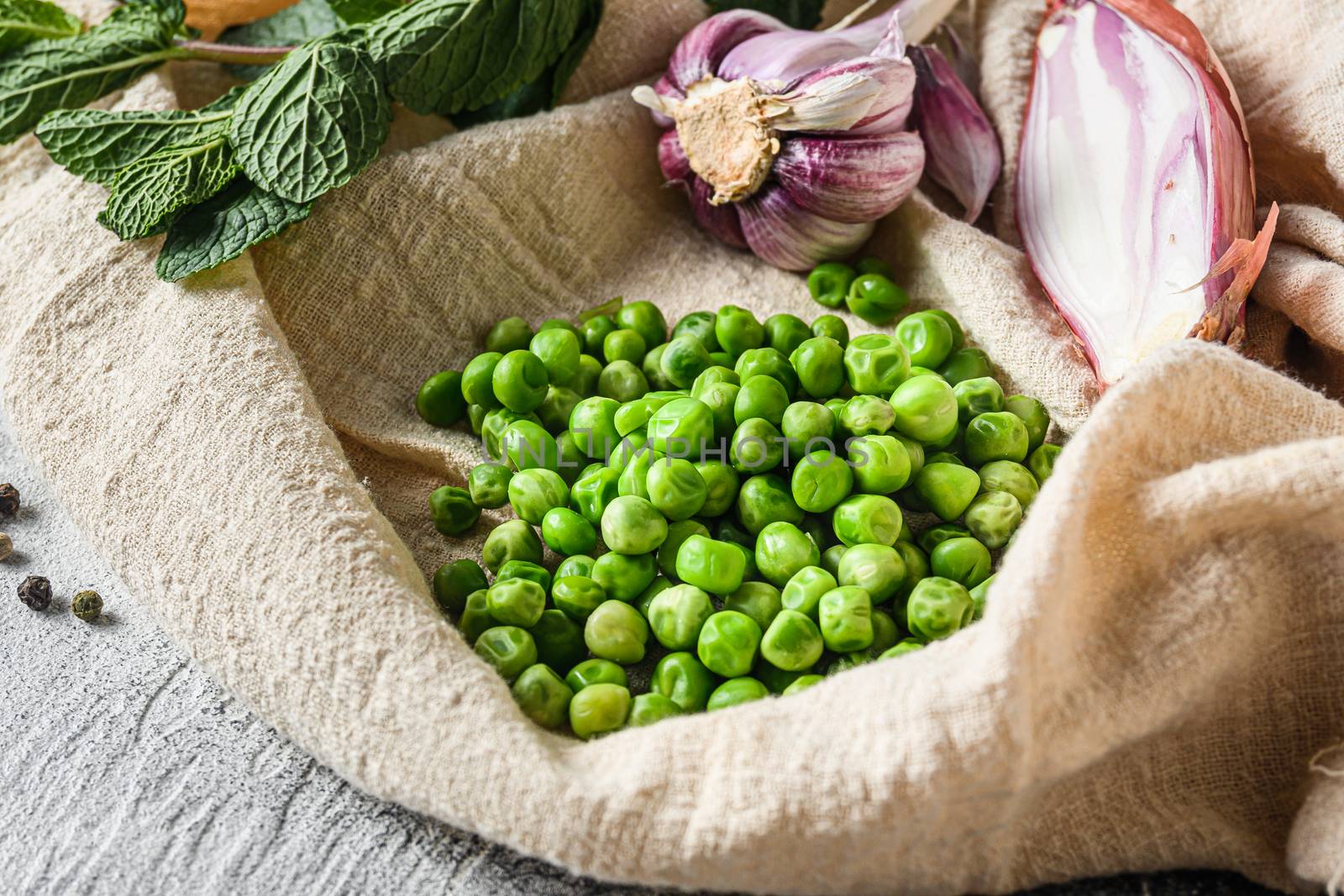 organic green peas for mushypeas and ingredients peas mint shallot pepper and salt keto food photo over grey stone background and cloth side view close up.