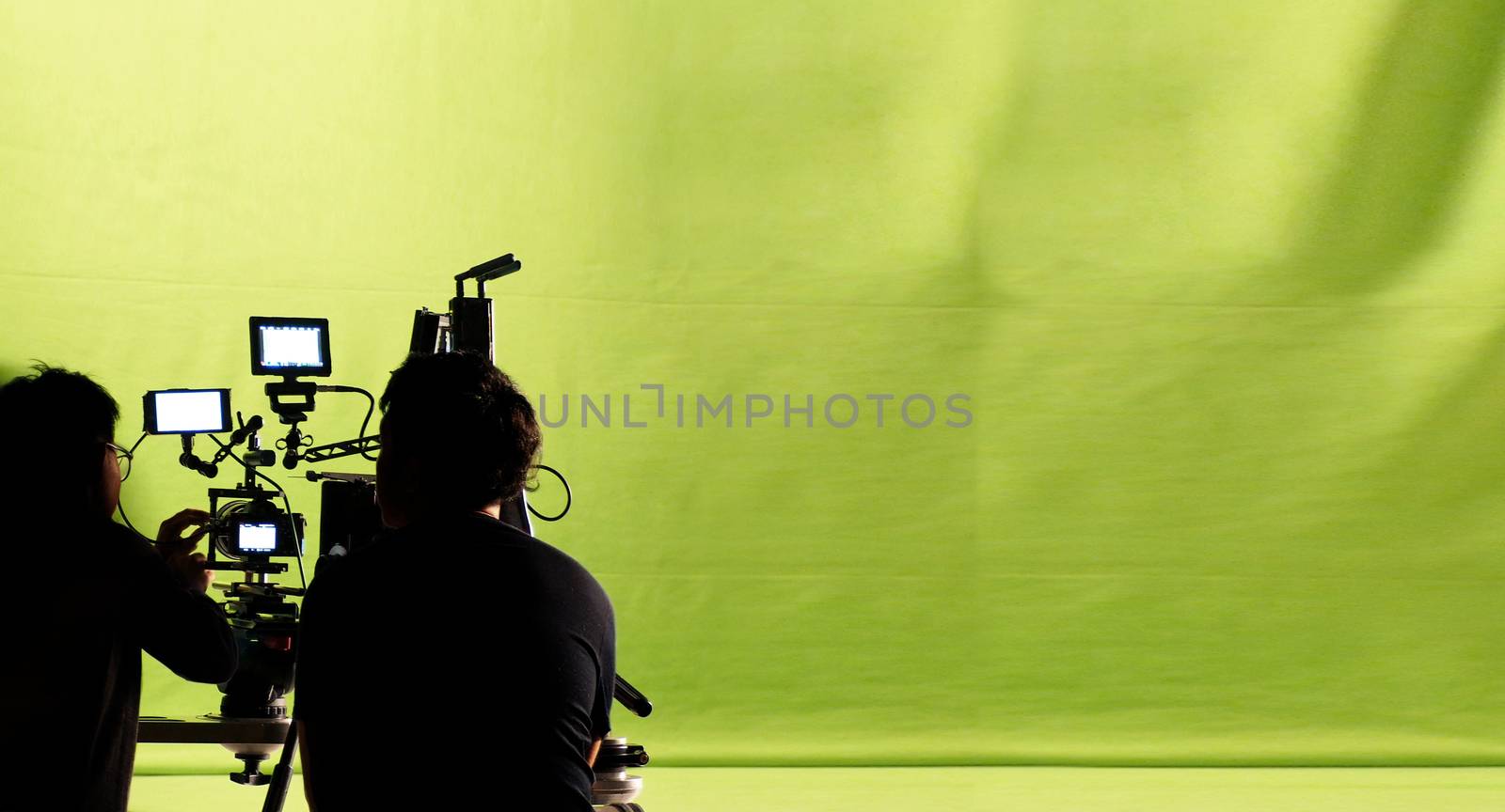 Behind the video production camera set and crew team shooting in a big green screen studio.